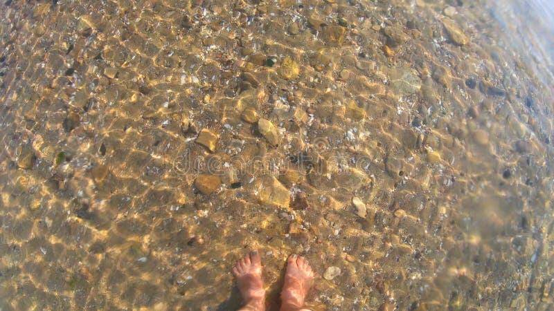 Femme debout pieds nus pieds pieds pieds pieds pieds pieds nus fond de mer sablonneux vagues d'eau transparente ondulent