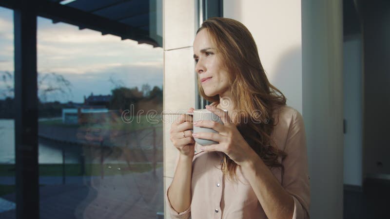 Femme décontractée rêvant près de la fenêtre après jour ouvrable Assez femme ayant le repos