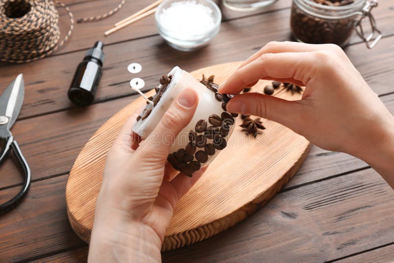 Femme décorant la bougie faite main avec des grains de café à la table en bois