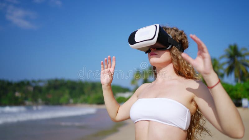 Femme en bikini ajuste la réalité virtuelle casque sur la plage explore le monde numérique. femelle au poil rond s'engage banque de vidéos
