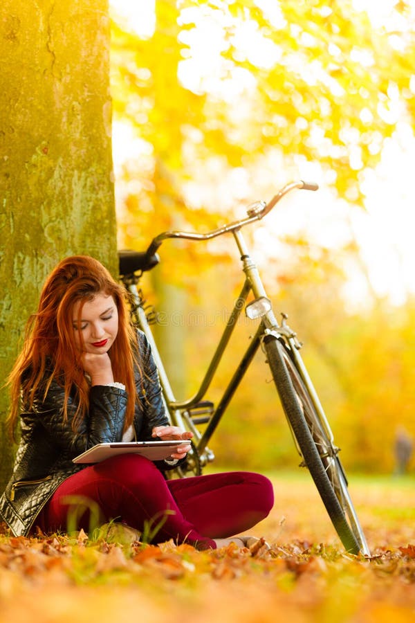 Femme dans un parc d'automne utilisant une tablette pour lire photographie stock libre de droits