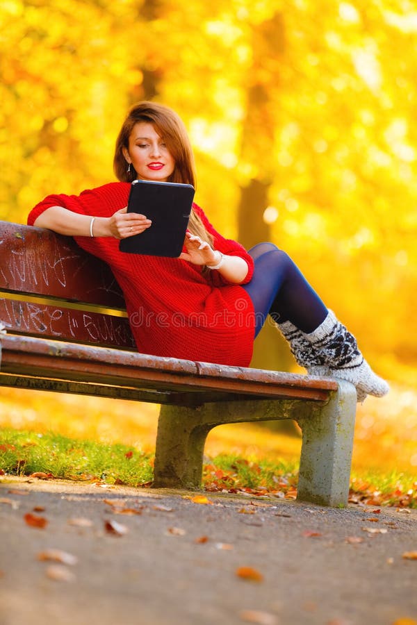 Femme dans un parc d'automne utilisant une tablette pour lire photo libre de droits