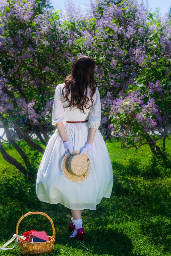Femme en robe blanche avec un chapeau de paille dans les mains dans une promenade dans le jardin image stock