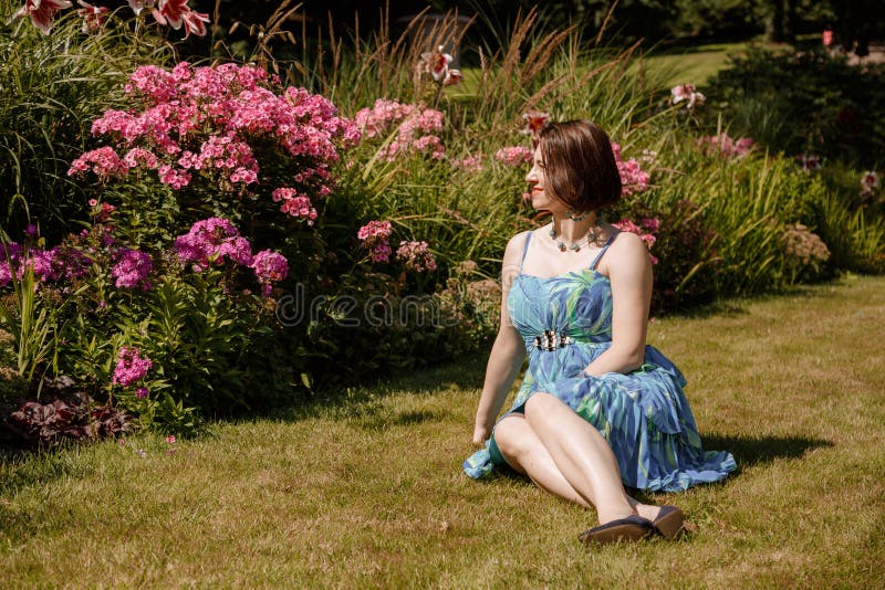 Femme en robe pose près des fleurs dans le jardin. fille brune assis sur un plaid dans le parc sur la nature. temps passé images stock