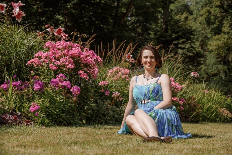 Femme en robe pose près des fleurs dans le jardin. fille brune assis sur un plaid dans le parc sur la nature. temps passé images libres de droits