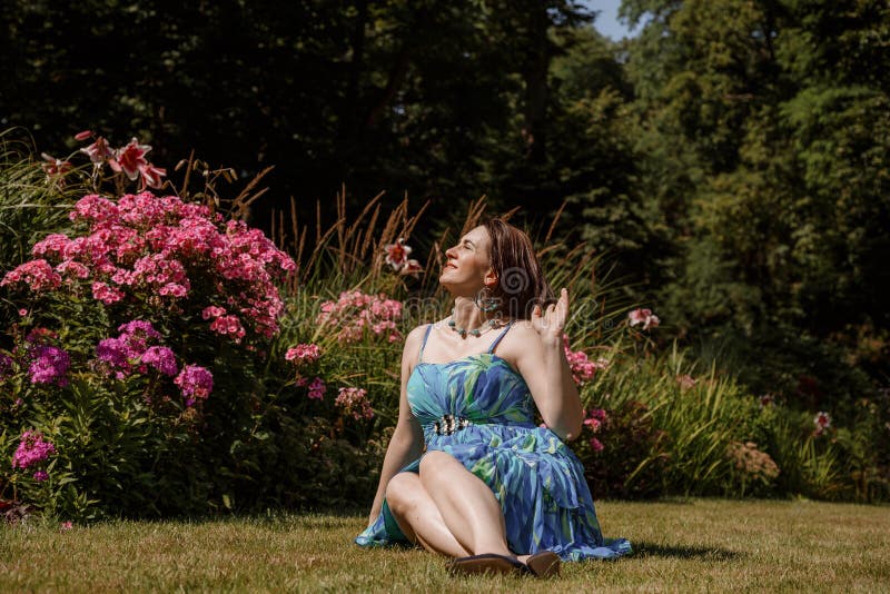 Femme en robe pose près des fleurs dans le jardin. fille brune assis sur un plaid dans le parc sur la nature. temps passé photo stock