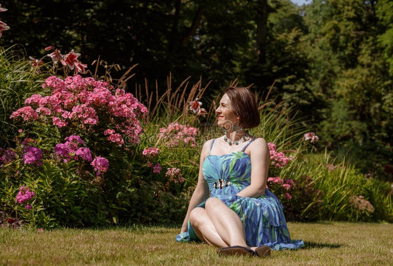 Femme en robe pose près des fleurs dans le jardin. fille brune assis sur un plaid dans le parc sur la nature. temps passé
