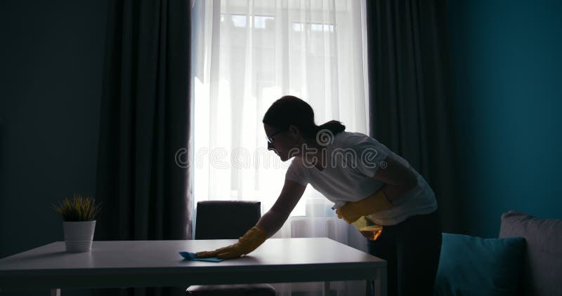 Femme en silhouette nettoyer la table en bois près de la fenêtre banque de vidéos