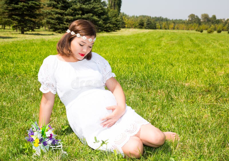 Femme enceinte asiatique heureuse avec le grand repos de ventre sur la nature photos stock Femme enceinte asiatique heureuse avec le grand repos de ventre sur la nature photos stock