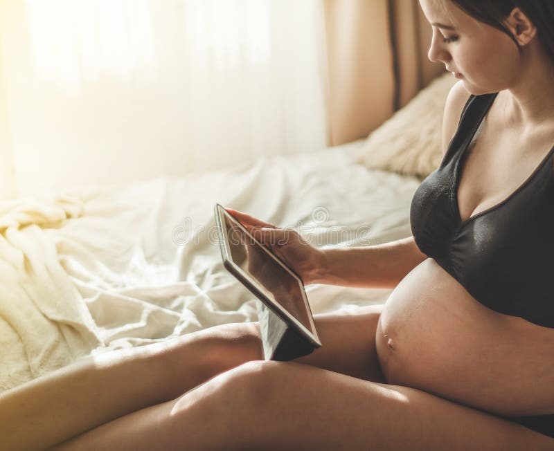 Femme enceinte avec le comprimé moderne se reposant sur le lit et ajustant ses longs cheveux Concept de grossesse et de technolo image libre de droits Femme enceinte avec le comprimé moderne se reposant sur le lit et ajustant ses longs cheveux Concept de grossesse et de technolo image libre de droits