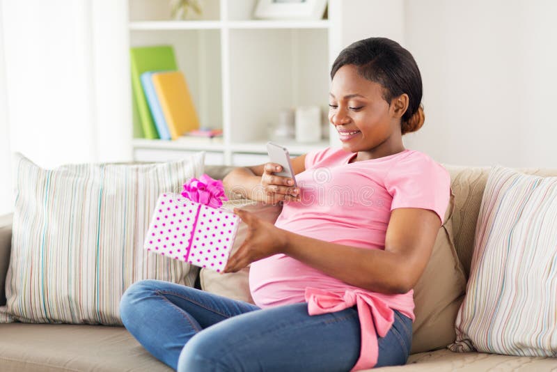 Femme enceinte d'Africain avec le smartphone et le cadeau image stock Femme enceinte d'Africain avec le smartphone et le cadeau image stock