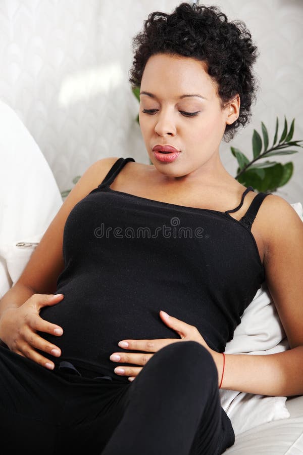 Femme enceinte de jeunes s'asseyant sur le sofa images stock Femme enceinte de jeunes s'asseyant sur le sofa images stock