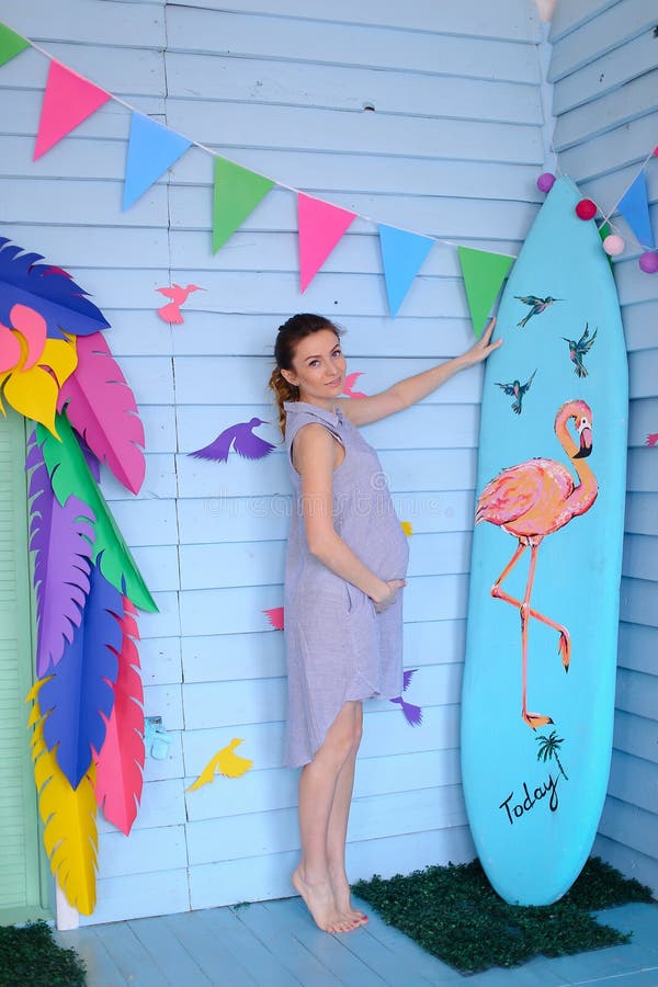 Femme enceinte de jeunes tenant la planche de surf proche et la maison décorée d'enfants images libres de droits Femme enceinte de jeunes tenant la planche de surf proche et la maison décorée d'enfants images libres de droits