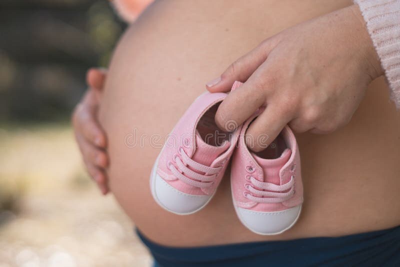 Femme enceinte en dehors de tenir des chaussures de bébé image stock Femme enceinte en dehors de tenir des chaussures de bébé image stock