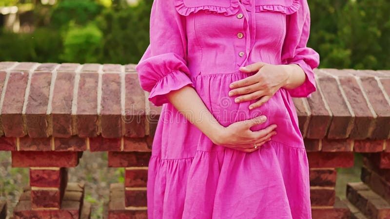 Femme enceinte en robe rose serrant le ventre dans le parc banque de vidéos