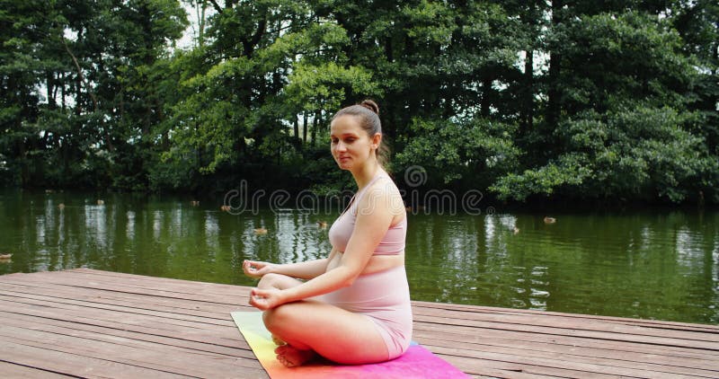 Femme enceinte faisant du yoga prénatal dans le parc près du lac exercices respiratoires pour accoucher banque de vidéos