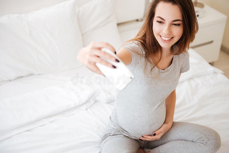 Femme enceinte gaie reposant et prenant le selfie avec le téléphone portable images stock Femme enceinte gaie reposant et prenant le selfie avec le téléphone portable images stock