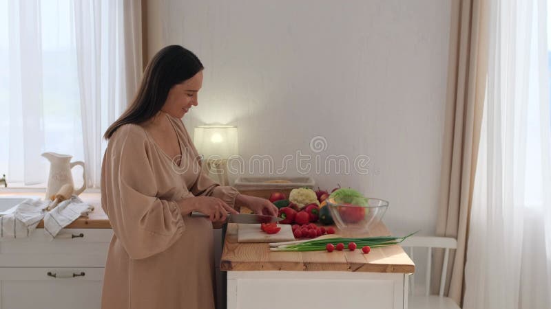 Femme enceinte joyeuse engagée dans la préparation de nourriture saine à la cuisine familiale banque de vidéos