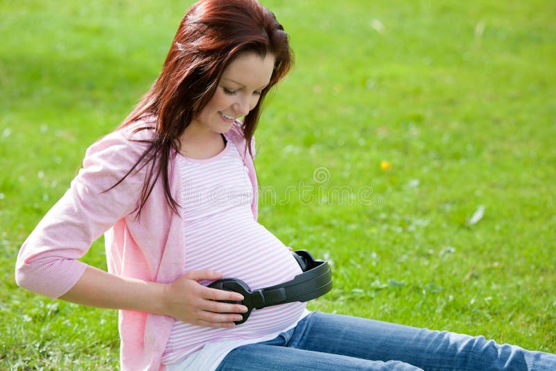 Femme enceinte mettant des écouteurs sur son ventre photos libres de droits Femme enceinte mettant des écouteurs sur son ventre photos libres de droits