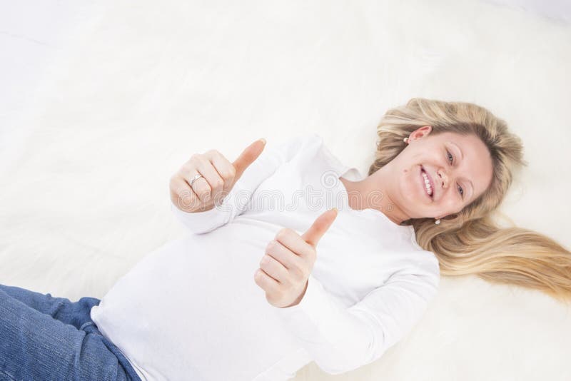 Femme enceinte s'étendant sur le tapis de fourrure dans la chemise et des jeans blancs image stock Femme enceinte s'étendant sur le tapis de fourrure dans la chemise et des jeans blancs image stock