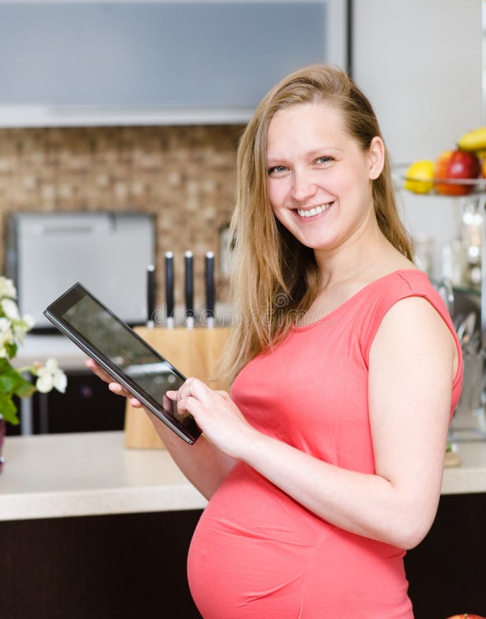 Femme enceinte à l'aide d'une tablette dans la cuisine image stock Femme enceinte à l'aide d'une tablette dans la cuisine image stock