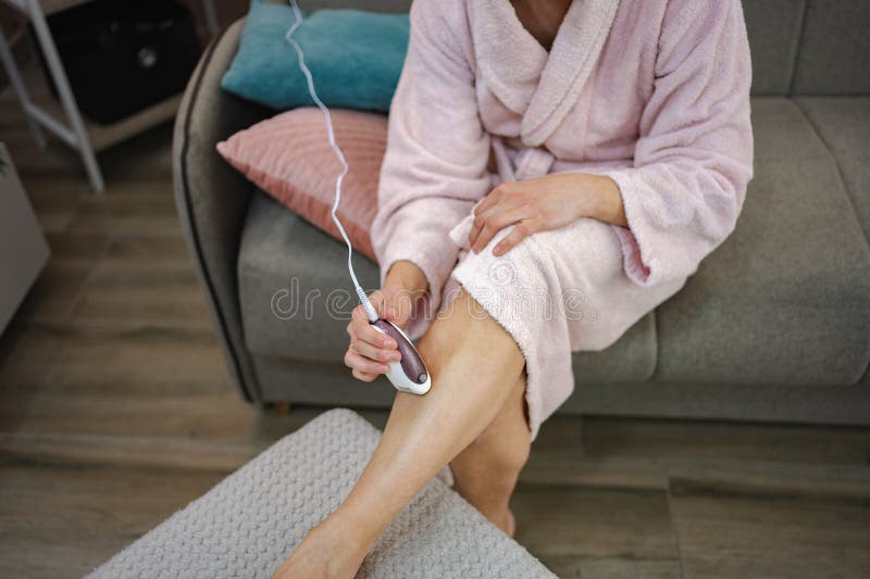 Femme enlever les cheveux de jambe avec épilateur électrique à la maison image stock
