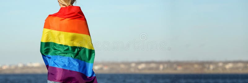 Femme enveloppée dans le drapeau lgbt clair près de la rivière vue arrière avec espace pour le texte. conception de bannières photographie stock libre de droits