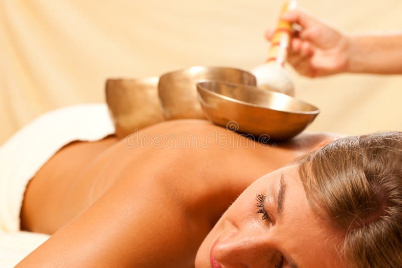 Woman in wellness and spa setting having a singing bowl therapy session. Woman in wellness and spa setting having a singing bowl therapy session