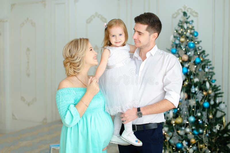 Femme européenne enceinte tenant le mari proche gardant la petite fille près de l'arbre de Noël photos libres de droits Femme européenne enceinte tenant le mari proche gardant la petite fille près de l'arbre de Noël photos libres de droits