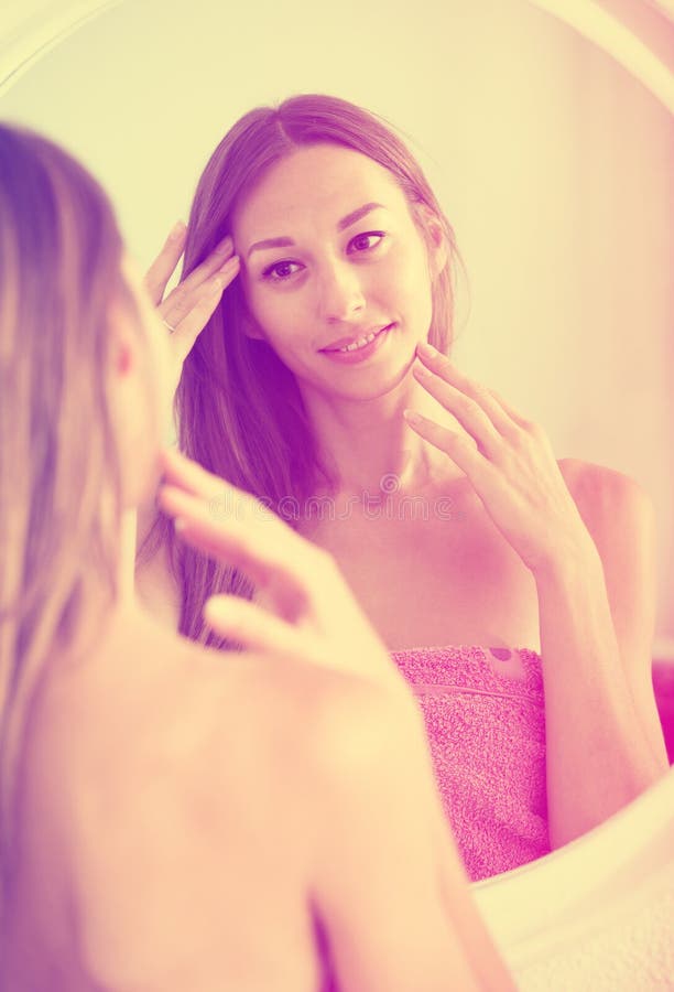 Femme examinant son visage en le regardant dans le miroir image stock Femme examinant son visage en le regardant dans le miroir image stock