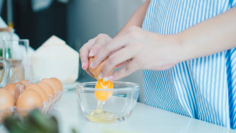Femme fendant un oeuf dans une cuvette avec se tenir prêt dans la cuisine photographie stock libre de droits Femme fendant un oeuf dans une cuvette avec se tenir prêt dans la cuisine photographie stock libre de droits
