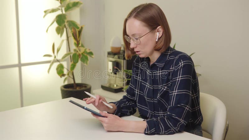 Femme focalisée avec écouteurs utilisant stylet pour annoter sur tablette dans bureau élégant. banque de vidéos