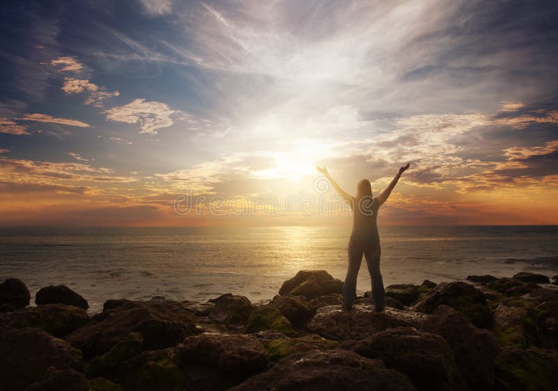 A woman standing at the ocean with her arms lifted in praise. A woman standing at the ocean with her arms lifted in praise