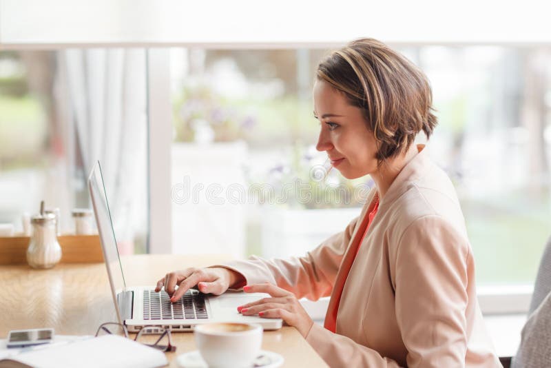 Femme gaie d'affaires dans le café dactylographiant sur l'ordinateur portable avec du café photos libres de droits Femme gaie d'affaires dans le café dactylographiant sur l'ordinateur portable avec du café photos libres de droits