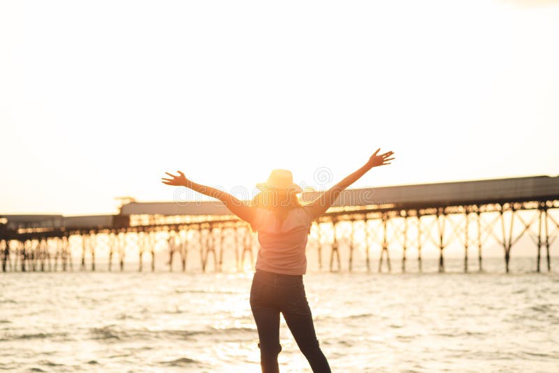 Femme heureuse avec des mains se levant sur la plage de coucher du soleil dans l'esprit d'été photos stock Femme heureuse avec des mains se levant sur la plage de coucher du soleil dans l'esprit d'été photos stock