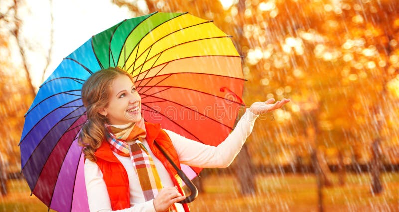 Femme heureuse avec le parapluie multicolore d'arc-en-ciel sous la pluie dans le pair