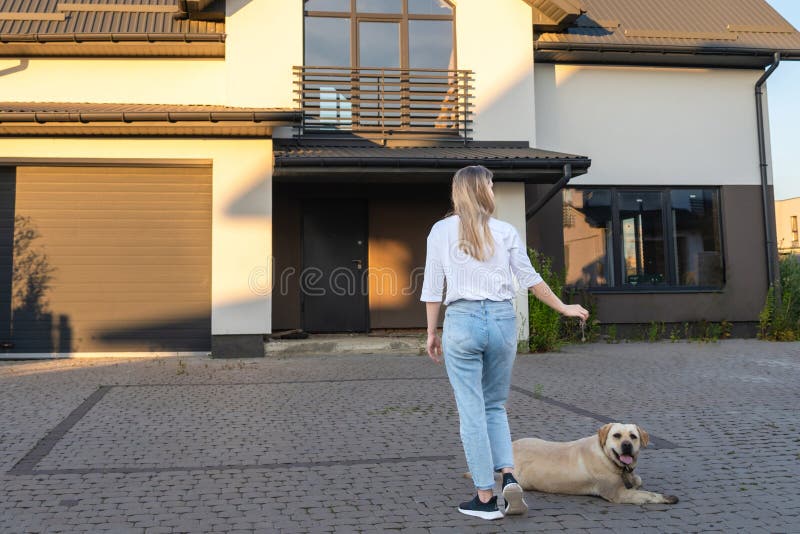 Femme heureuse avec un chien debout avec les clés de la maison devant la maison résidentielle. location immobilière pour réinstall photos stock