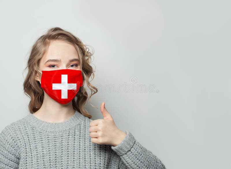 Happy woman in face mask holding thumb up with Switzerland flag background. Flu epidemic and virus protection concept. Happy woman in face mask holding thumb up with Switzerland flag background. Flu epidemic and virus protection concept.