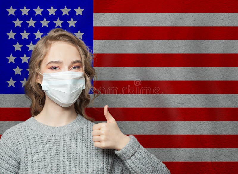 Happy woman in face mask holding thumb up on national flag USA  background. Flu epidemic and virus protection concept. Happy woman in face mask holding thumb up on national flag USA  background. Flu epidemic and virus protection concept.