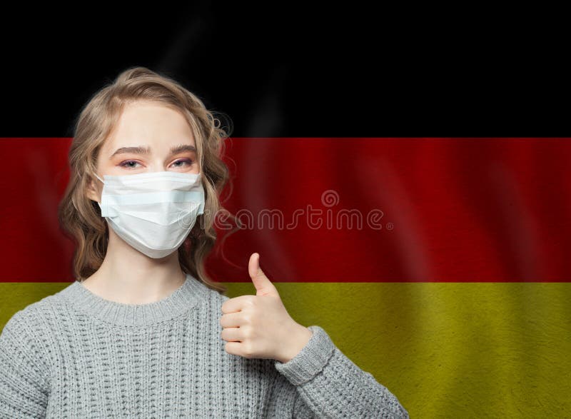 Happy woman in face mask holding thumb up on national flag Germany background. Flu epidemic and virus protection concept. Happy woman in face mask holding thumb up on national flag Germany background. Flu epidemic and virus protection concept.