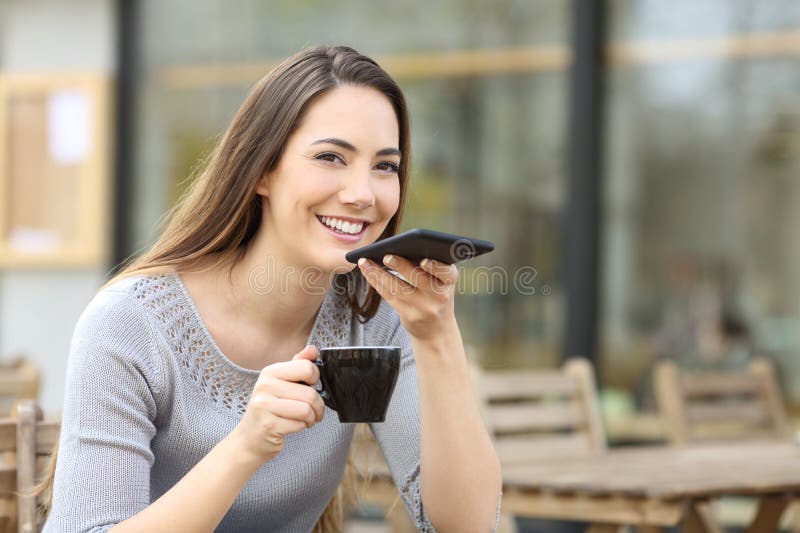 Femme heureuse dans une terrasse bar dictant le message sur le téléphone photos libres de droits