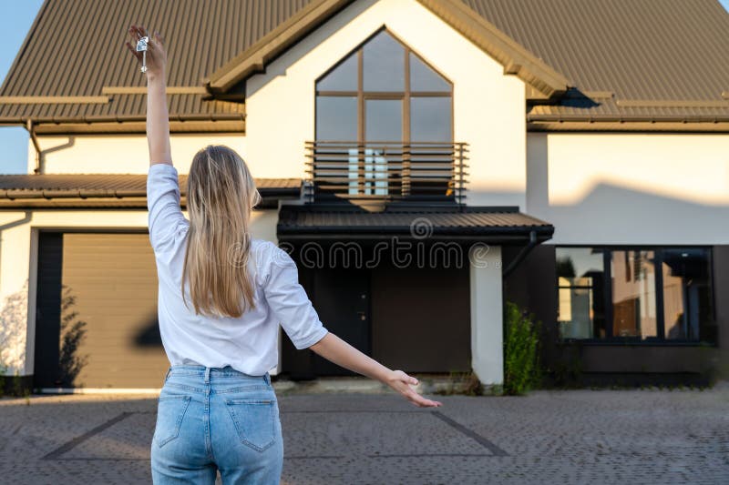 Femme heureuse debout avec les clés de la maison devant la maison résidentielle. immobilier déménagement ou location concept immob photo stock