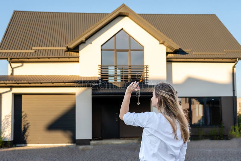 Femme heureuse debout avec les clés de la maison devant la maison résidentielle. location immobilière pour réinstallation. assuran photographie stock