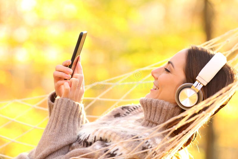 Femme heureuse écoutant de la musique sur hamac en automne images libres de droits