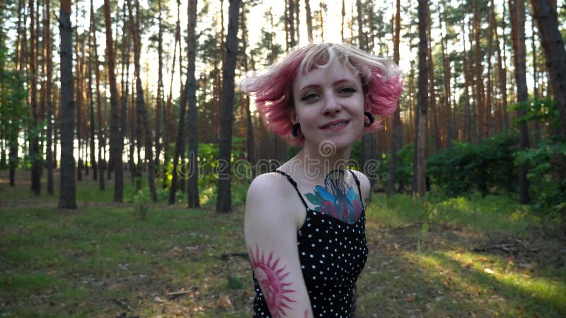 Femme hippie insouciante avec tatouages sur le chemin de la forêt. fille punk souriante heureuse avec cheveux roses regardant vers banque de vidéos