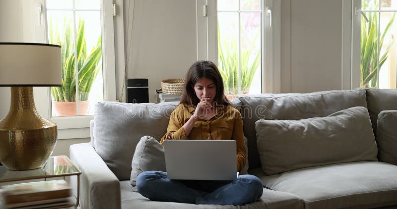 Femme hispanique sérieuse assise sur un canapé avec ordinateur portable clips vidéos