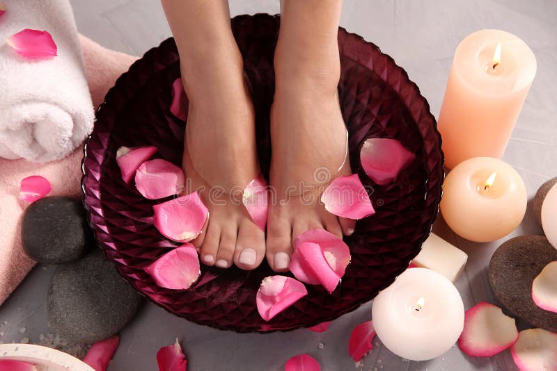 Femme imbibant de ses pieds dans la cuvette l'eau et des p? tales de rose sur le plancher gris photo stock
