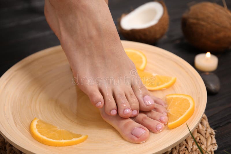 Femme imbibant de ses pieds dans le plat l'eau et tranches oranges sur le plancher en bois, plan rapproché photographie stock