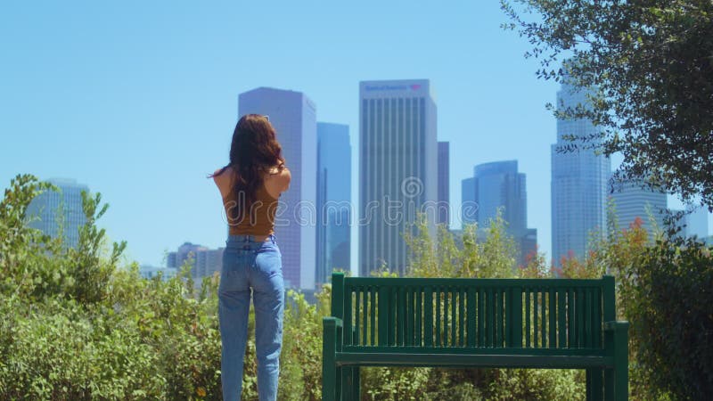 Femme inconnue debout dans le parc faisant des gratte-ciel photo sur smartphone vue arrière. banque de vidéos