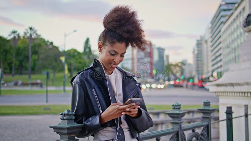 Femme joyeuse messagerie cellulaire se penchant sur les rampes urbaines à la fermeture du soir. banque de vidéos